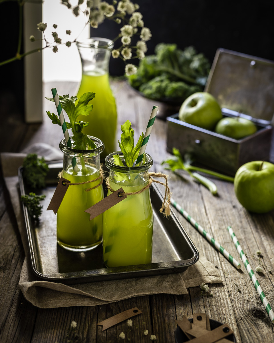 Green apple and kale juice in a moody scene by an open door with apples in the background