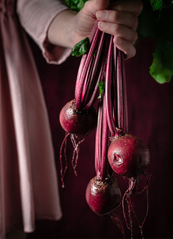 A hand holding a bunch of freshly harvested beetroot