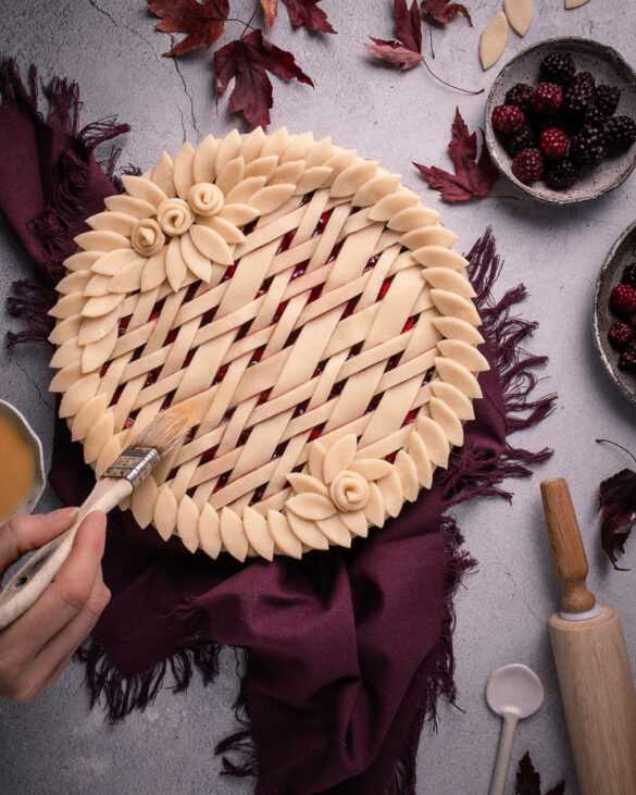 A blackberry pie with dough leaves around the edge and a woven criss cross pattern