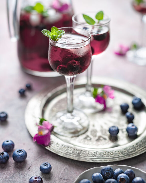 A silver tray with two glasses of blueberry iced tea and a few scattered blueberries
