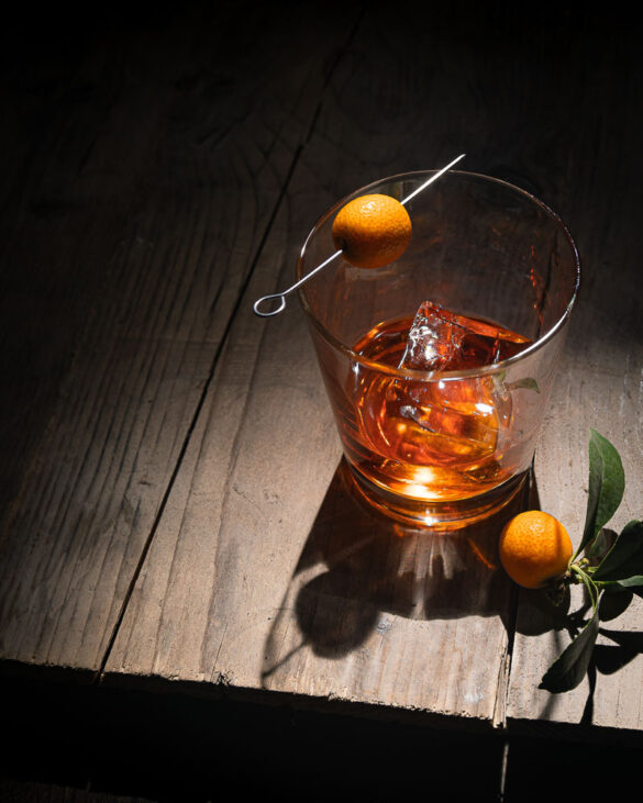 A moody wooden table scene with a glass of negroni with cumquats as decoration