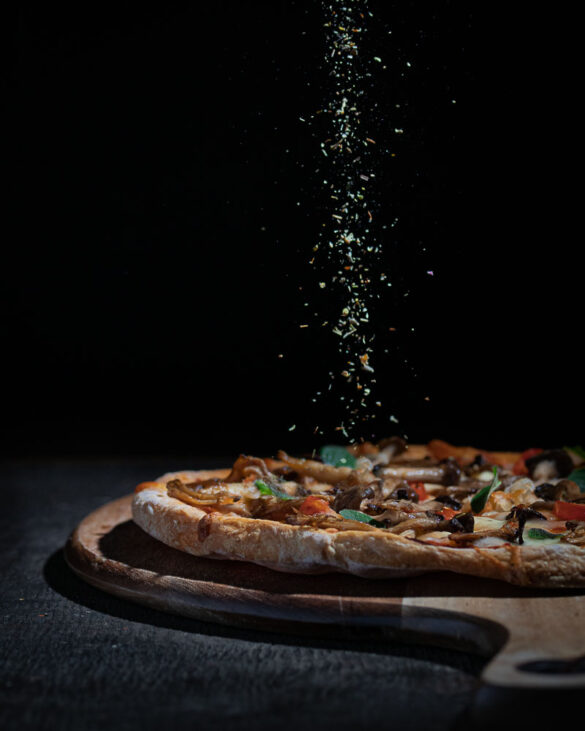 A rustic pizza on a board being sprinkled with a herb and salt mix