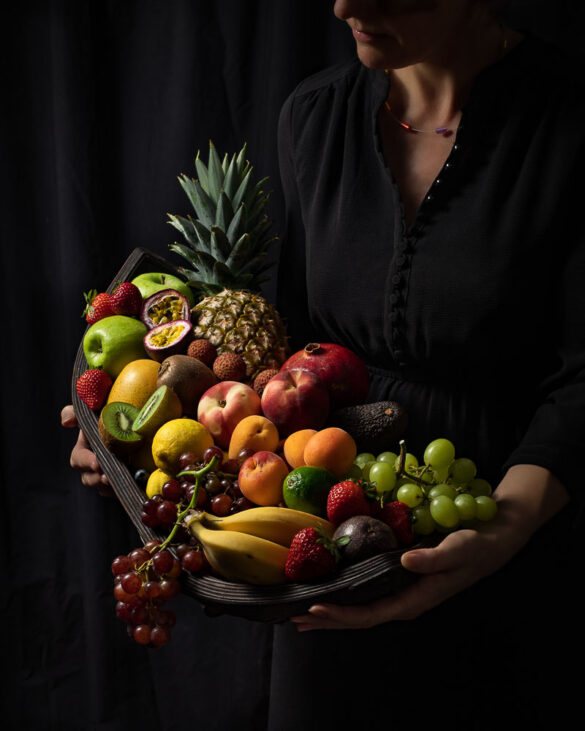 A woman holding a large, boat-shaped bowl filled with all sorts of fruit