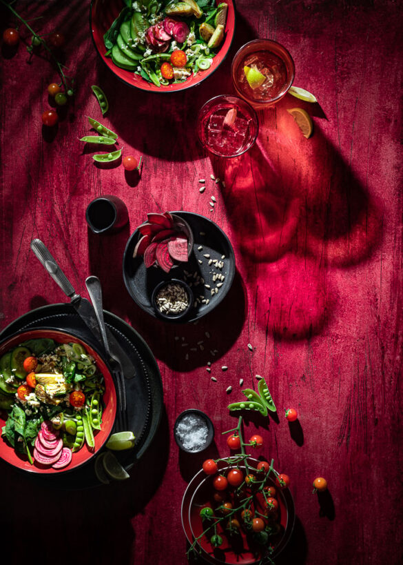 A very red scene with two plates of garden salad, and two red glasses casting long shadows
