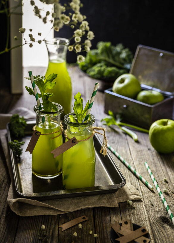 Green apple and kale juice in a moody scene by an open door with apples in the background
