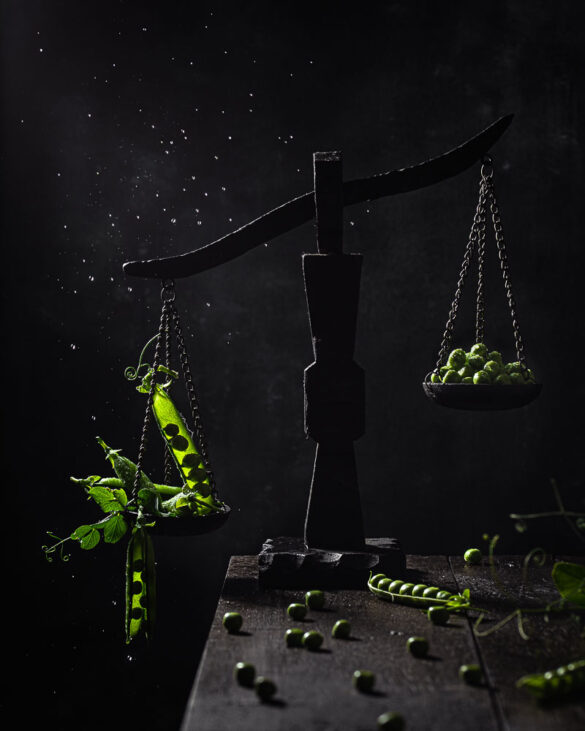 A very dark scene of an old fashioned scale with green peas shelled and unshelled