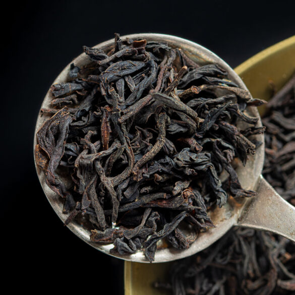 A macro shot of a round spoon holding black tea leaves