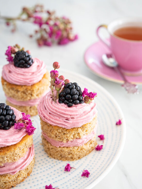 Three Earl grey blackberry bites on a white plate with a pink cup of tea and pink flowers in the background