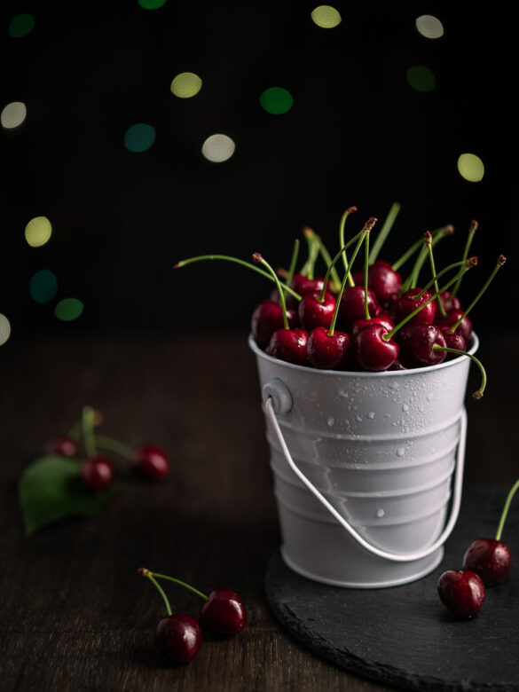 A small white bucket of cherries with green bokeh in the background