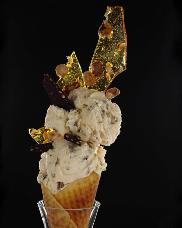Two scoops of ice cream mixed with nuts and chocolate, held in a homemade waffle cone, decorated with shards of see-through yellow caramel