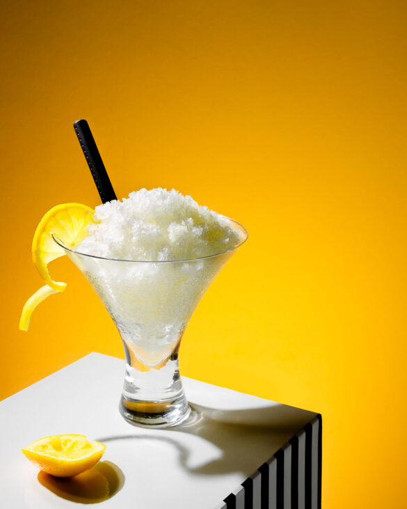 A V-shaped glass with lemon granita in front of bright yellow background