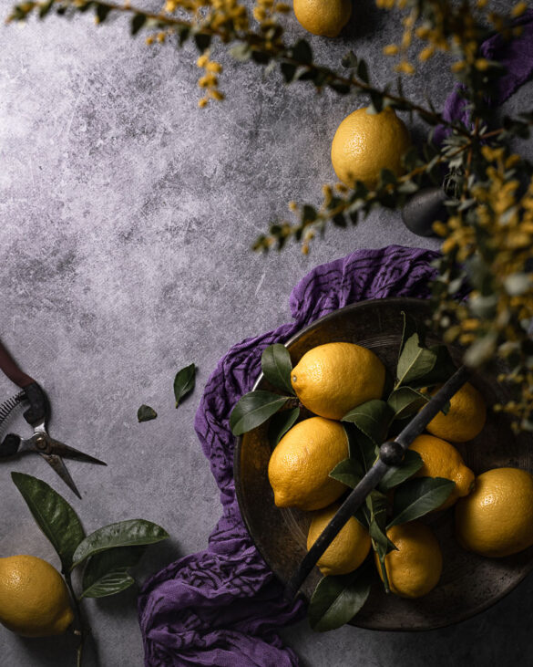 Still life of yellow lemons on purple surface with purple scarf and yellow flours