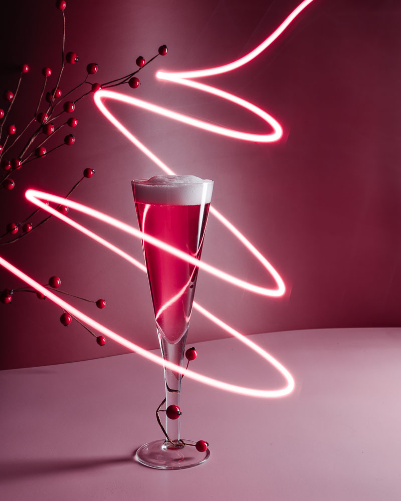 A champagne glass with a raspberry sour with light painting swirling around it