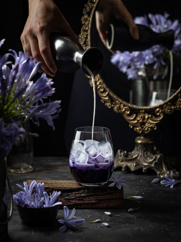 Milk being poured into a glass of purple cordial in front of an enchanted mirror