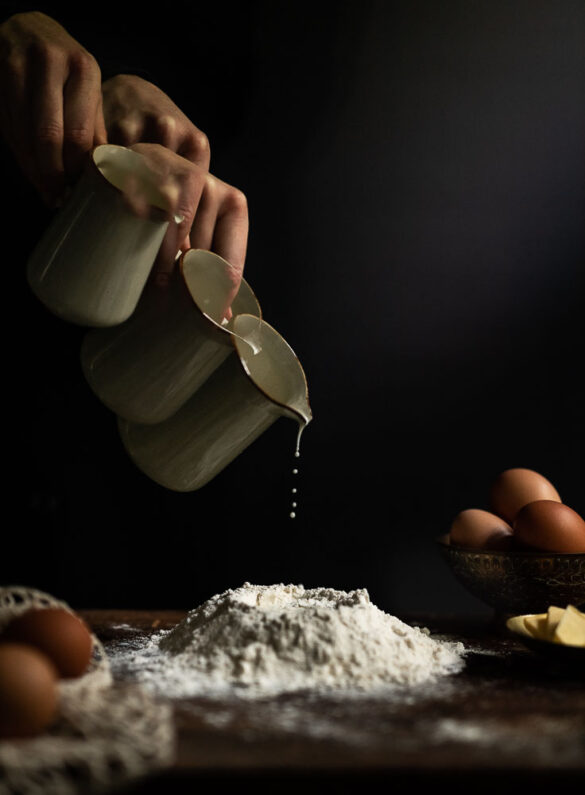 Multiple exposure shot of a hand holding a jug and pouring milk into a mountain of flour on a table