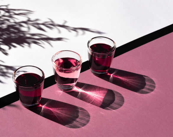 three pink shot glasses in the sun on a pink background creating dramatic shadows