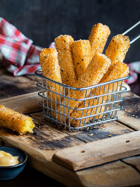 A metal basket of crispy fried polenta chips on a wooden board with a check serviette