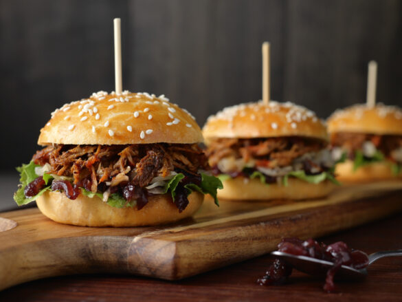 Three pulled pork sliders with a skewer through the top on a wooden board