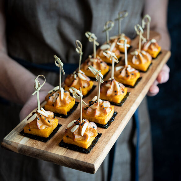 A person holding a board of pumpkin canapes on seaweed squares