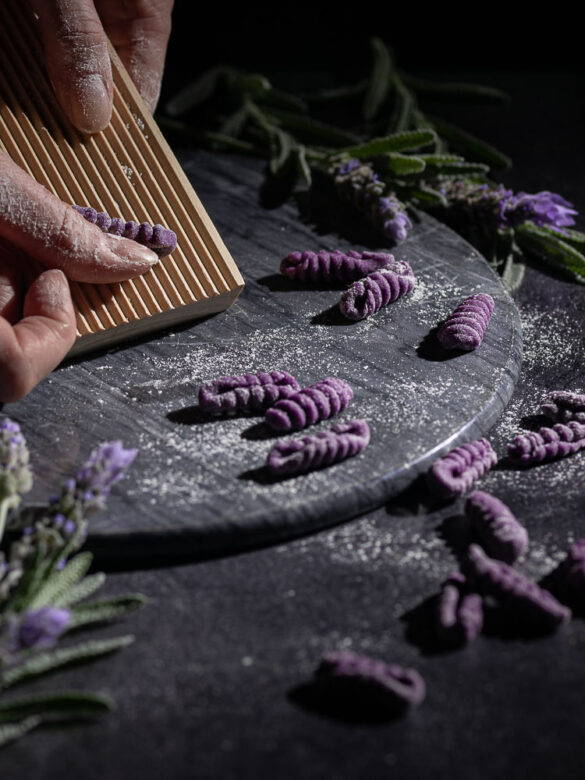 A scene of purple cavatelli being made on a gnocchi board
