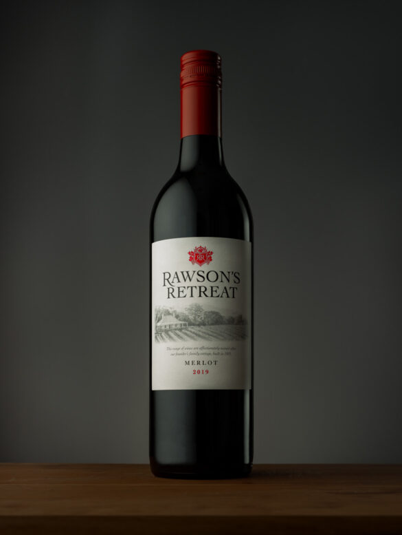 A bottle of Rawson's Retreat wine on a wooden surface in front of a grey background