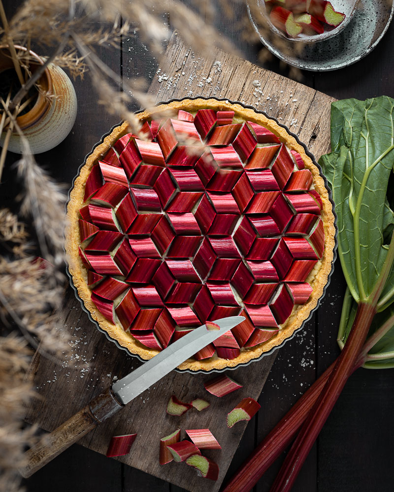 An intricate pattern made with rhubarb on a tart, with fresh rhubarb on the side