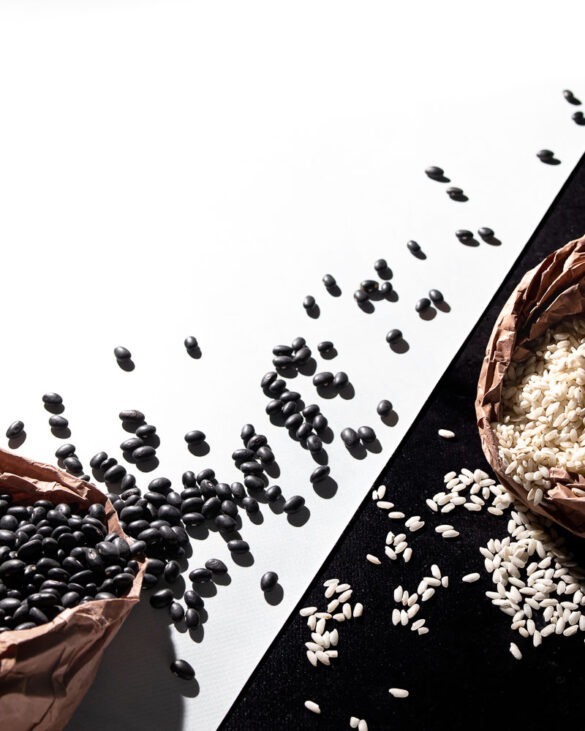 Artistic scene of a brown bag of black beans spilling out on a white background, and a brown bag of white rice spilling out on a black background