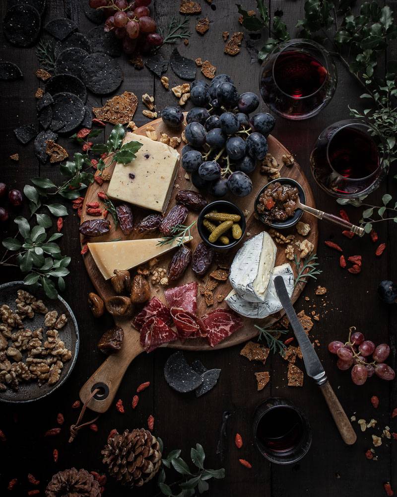 Overhead shot of a rustic cheese board with wine, grapes and crackers around it