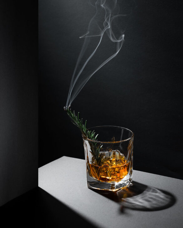 A brandy with a twig of burning rosemary creating smoke