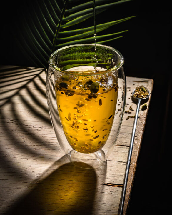 A backlit class cup of yellow spice tea with a fern casting a shadow on the table