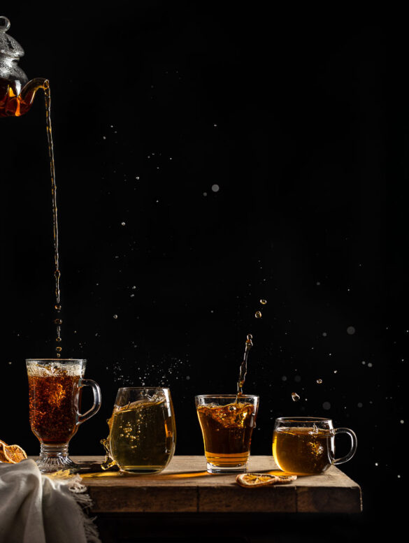 Four glasses of tea lined up on a table, all with splashes
