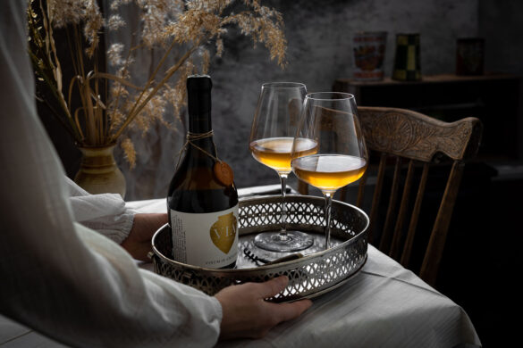 A silver tray of yellow wine in two glasses and a bottle of Vinum in Amphorae being placed onto a table with a white tablecloth