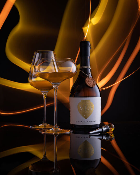 Two beautiful glasses of golden wine and a bottle of Vinum in Amphorae in front of yellow light painting