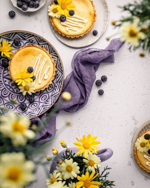 Little yellow vanilla cheesecakes on a purple plate with a purple napkin and yellow flowers