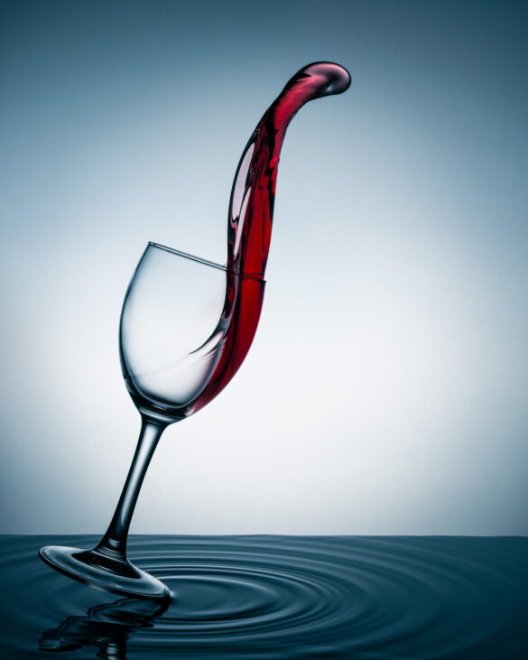 A glass of wine lightly touching the surface of a body of water with a large tongue of wine swooshing out the top