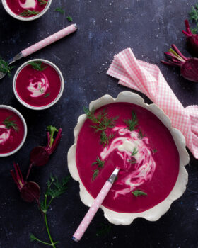 Pretty bowl of bright pink beetroot soup with light pink spoons and dill garnish