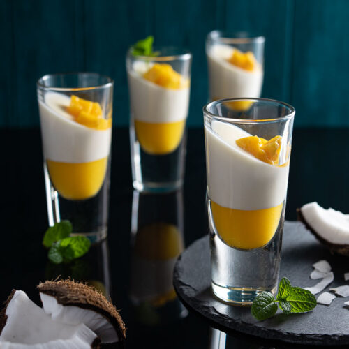 Four glasses layered with mango puree and coconut panna cotta
