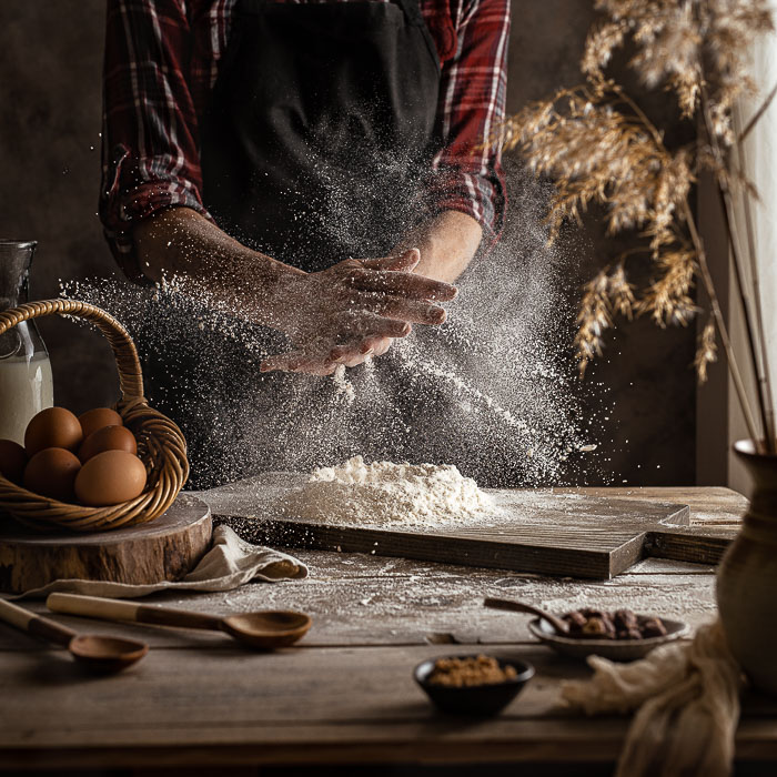 A baking scene with two hands clapping and flour flying everywhere