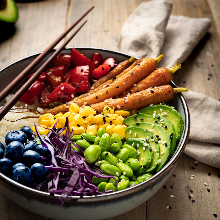 A close up of a poke bowl with corn, carrot, avocado, capsicum, blueberries, edamame and cabbage